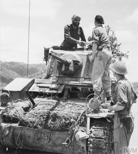 Sikh and British troopers shake hands on a tank.